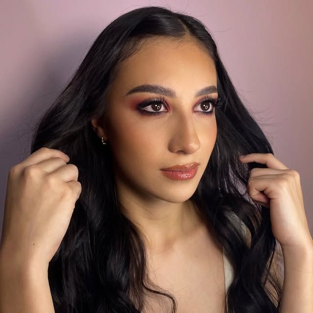 Maquillaje cálido con ondas largas en cabello negro.